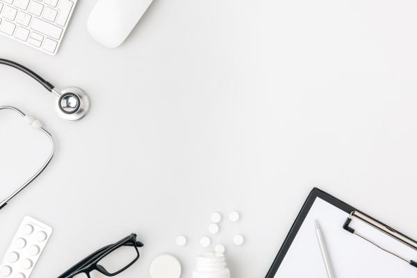 Photo of partial keyboard, flipboard, pen, black rimmed glasses and stethoscope on a white background
