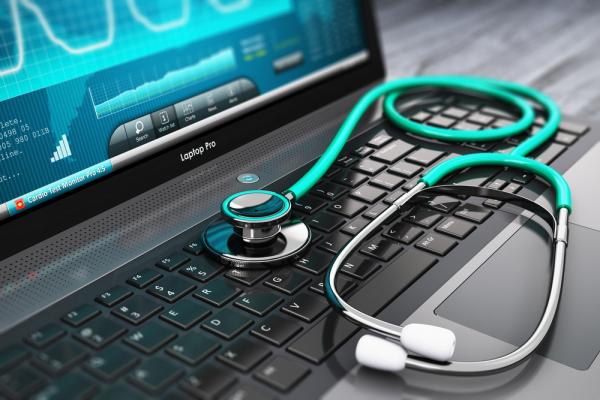 Photo of a computer with a blue chart on the screen. On top of the keyboard lies a green and silver stethoscope