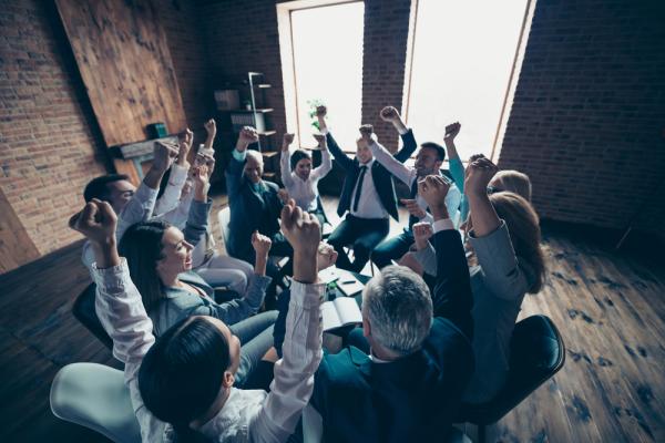 In a workplace setting, a team raise their hands in celebration their jobs at Keypath.