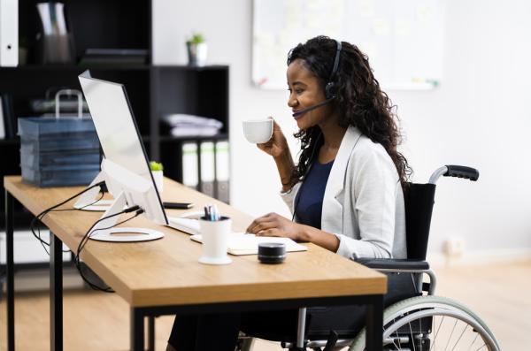 Stock photo of disabled woman in a wheelchair having a cup of tea while smiling at her computer screen
