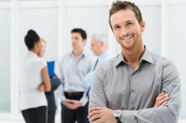 A young office worker smiles as his colleagues stand behind him in the group and chat
