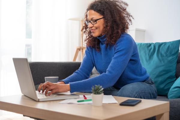 A woman sits down on her couch in front of a laptop to find out how to study while working full time.