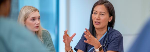In a meeting with colleagues, a nurse gestures with her hands to emphasize the point she is discussing on working collaboratively to deal with staff shortages.
