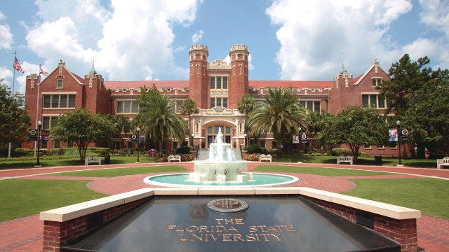 A sign reading "The Florida State University" sits in front of a fountain and red brick campus building.