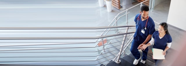 A diverse pair of young nurses walks up the hospital stairs while engrossed in conversation.