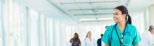 Confident young Hispanic nurse looks to the side while walking in a hospital corridor.